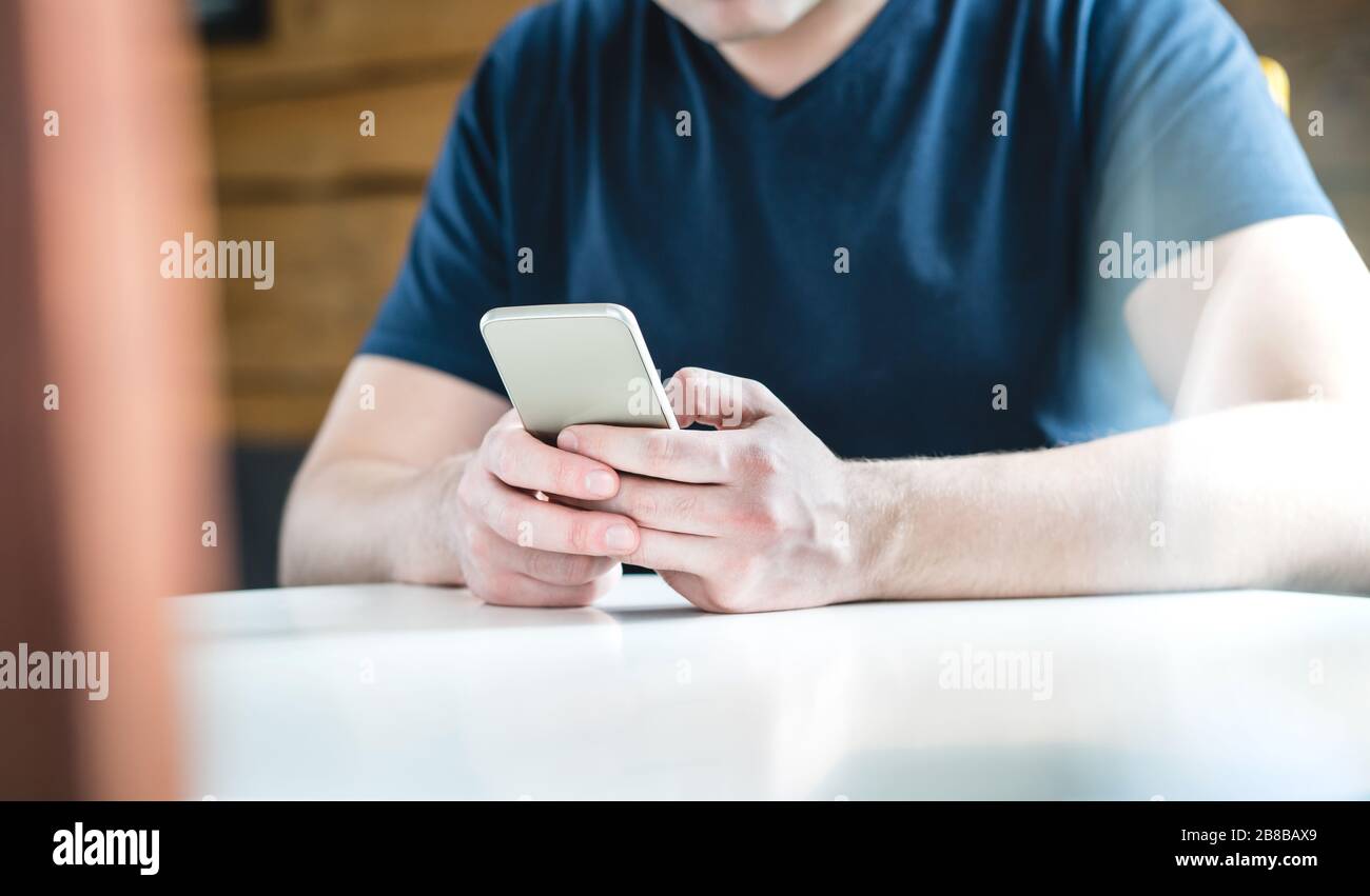 Young man texting with smartphone. Guy using mobile phone against wooden wall and background. Cropped close up shot of hands holding cellphone. Stock Photo