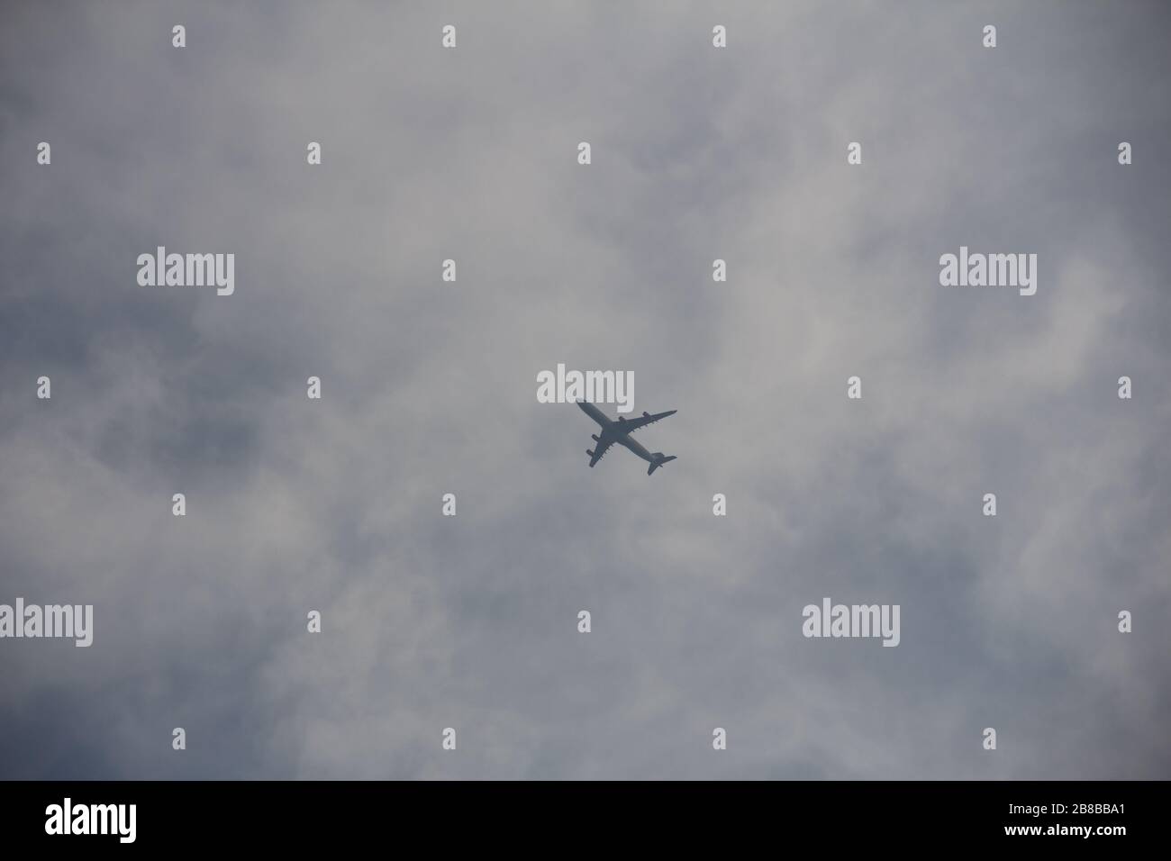 A single plane is seen from below as it tries to pass the thick clouds on a dark summer day Stock Photo