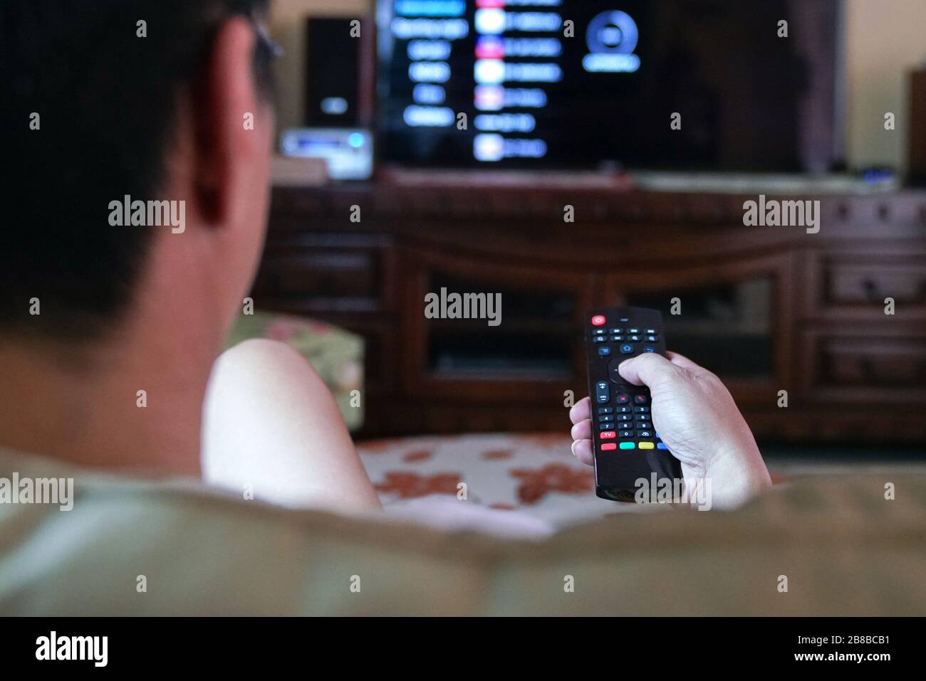 Man watching tv with focus on his hands on the remote control. Home entertainment or stay at home concept. Stock Photo