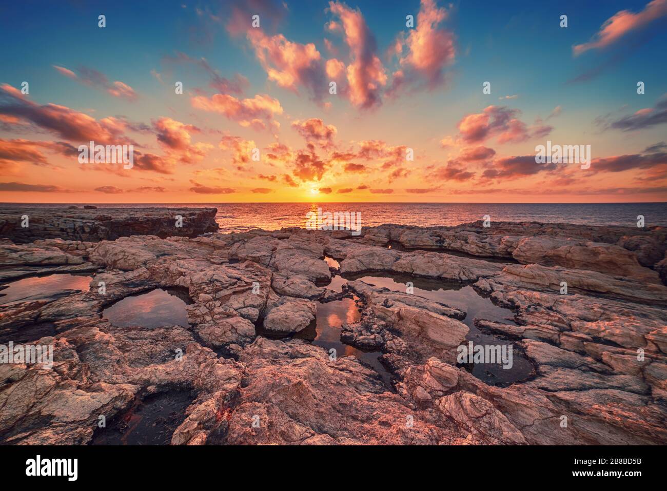 Beautiful colorful sunset near the sea at Cyprus with dramatic clouds and boulders. Reflections in the water. Beauty world natural outdoors travel background Stock Photo