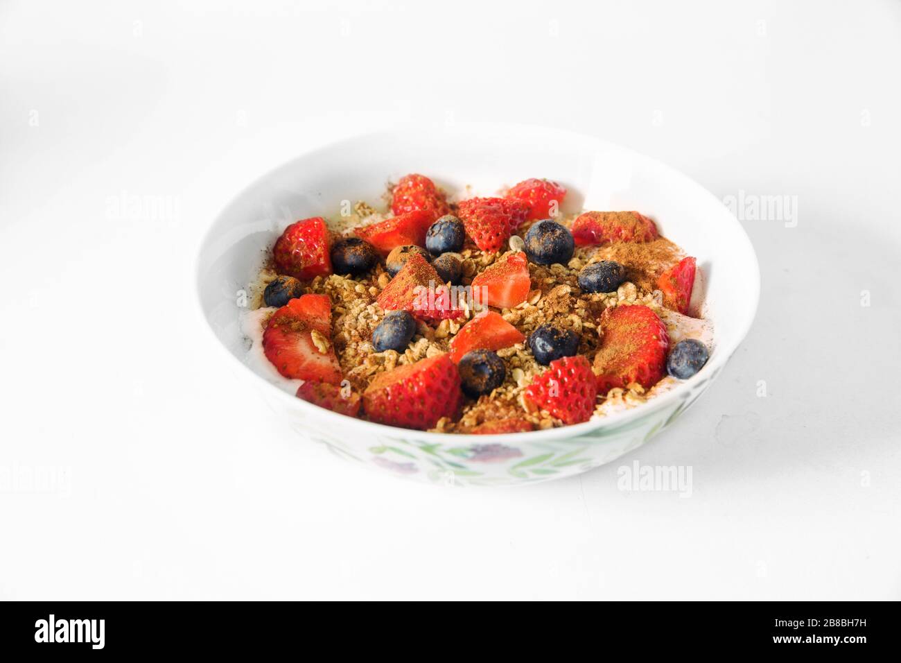 A Healthy Happy Oatmeal Breakfast for a time of isolation. A Bowl of oats, granola, strawberry, blueberries, yogurt, with white bowl, white background Stock Photo