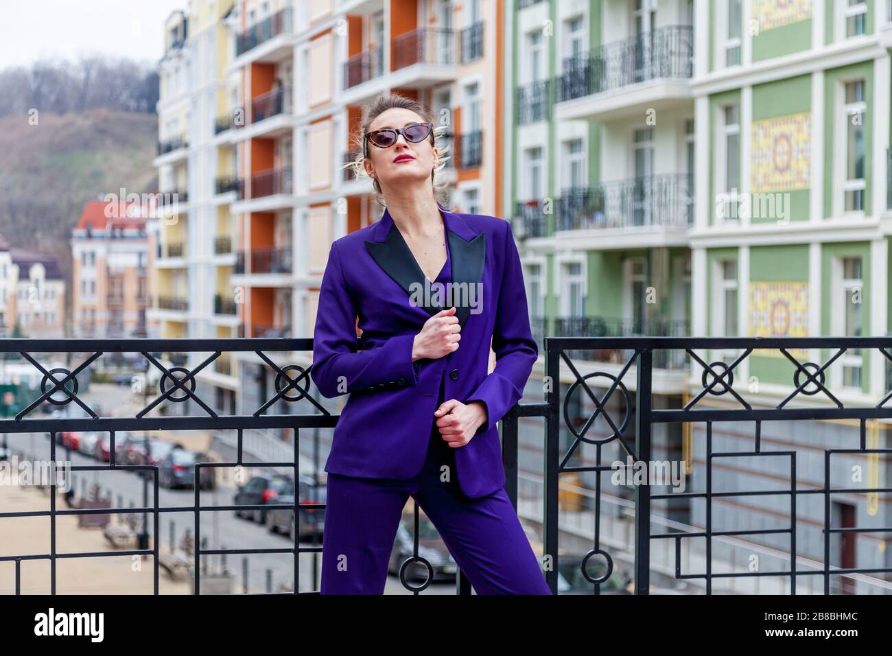 A portrait of a blond woman wearing in a purple suit and glasses poses ...