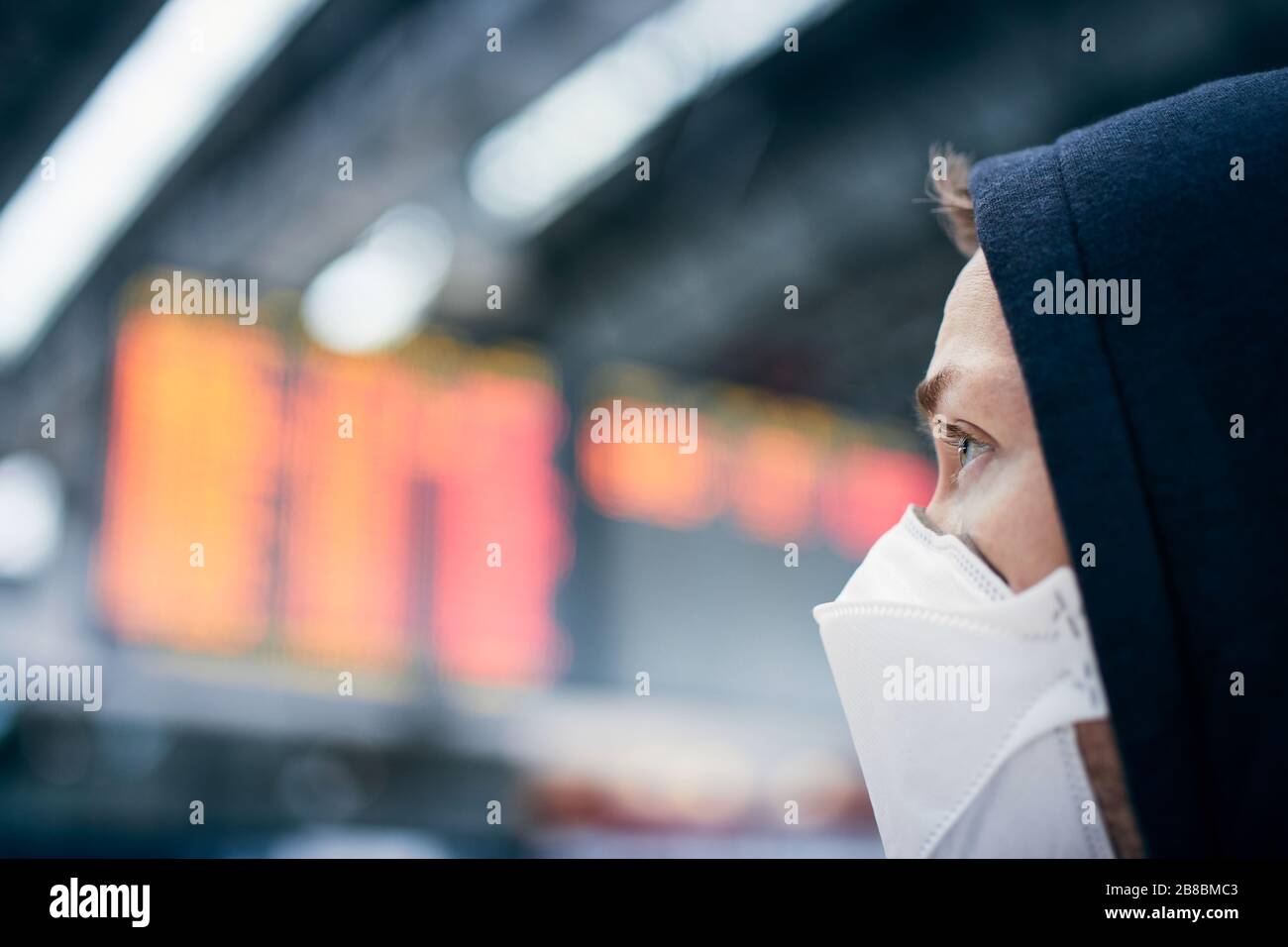 Man wearing face mask against airport departure board. Themes coronavirus, canceled flights and personal protection. Stock Photo