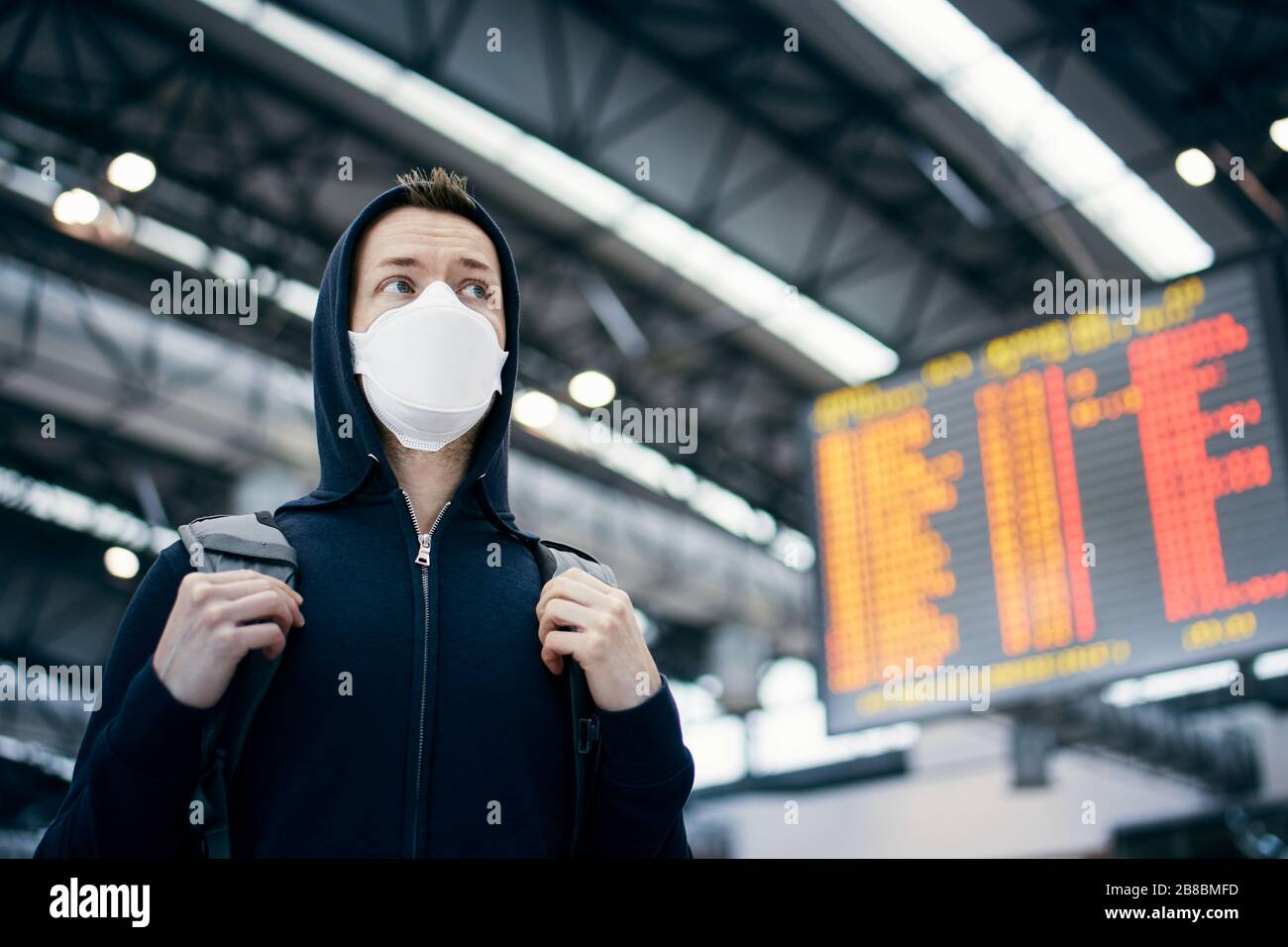 Man wearing face mask against airport departure board. Themes coronavirus, canceled flights and personal protection. Stock Photo