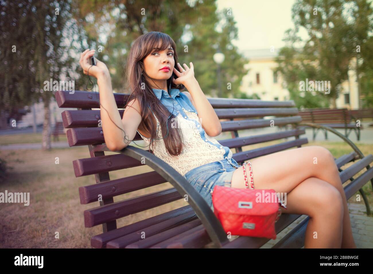 Side view of beautiful girl with long hair listening to music on mp3 player  and singing. Charming lady sitting on bench and enjoying favorite songs. C  Stock Photo - Alamy