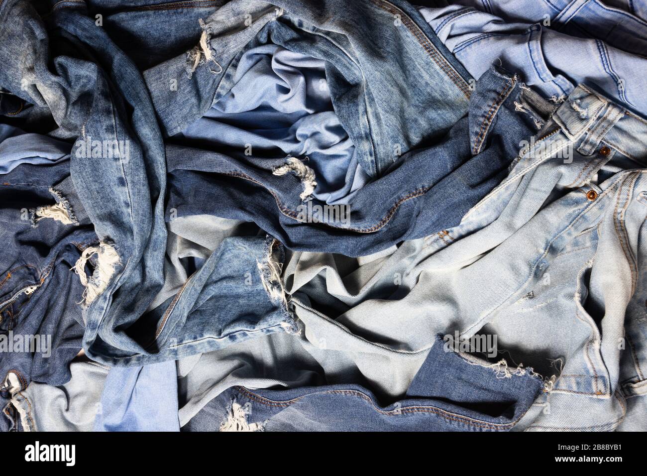 Different blue colored female jeans mixed, messy pile of navy jeans