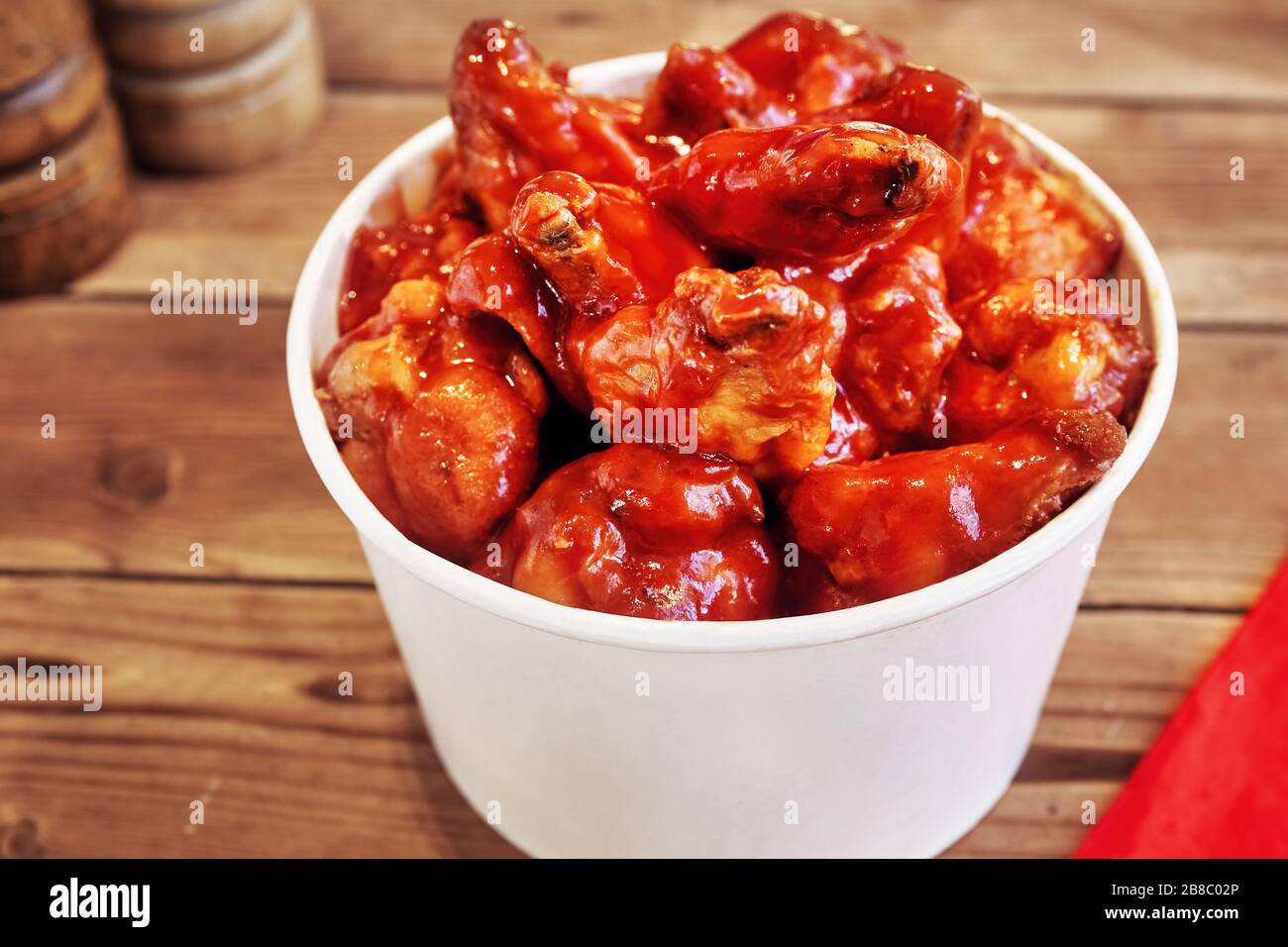 Bucket of chicken wings with hot chili sauce on wooden table Stock Photo