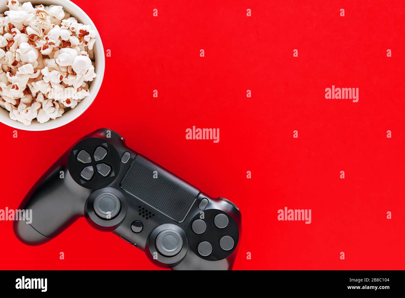 Bowl of popcorn with a gamepad on a red background. Play console games in  leisure time Stock Photo - Alamy