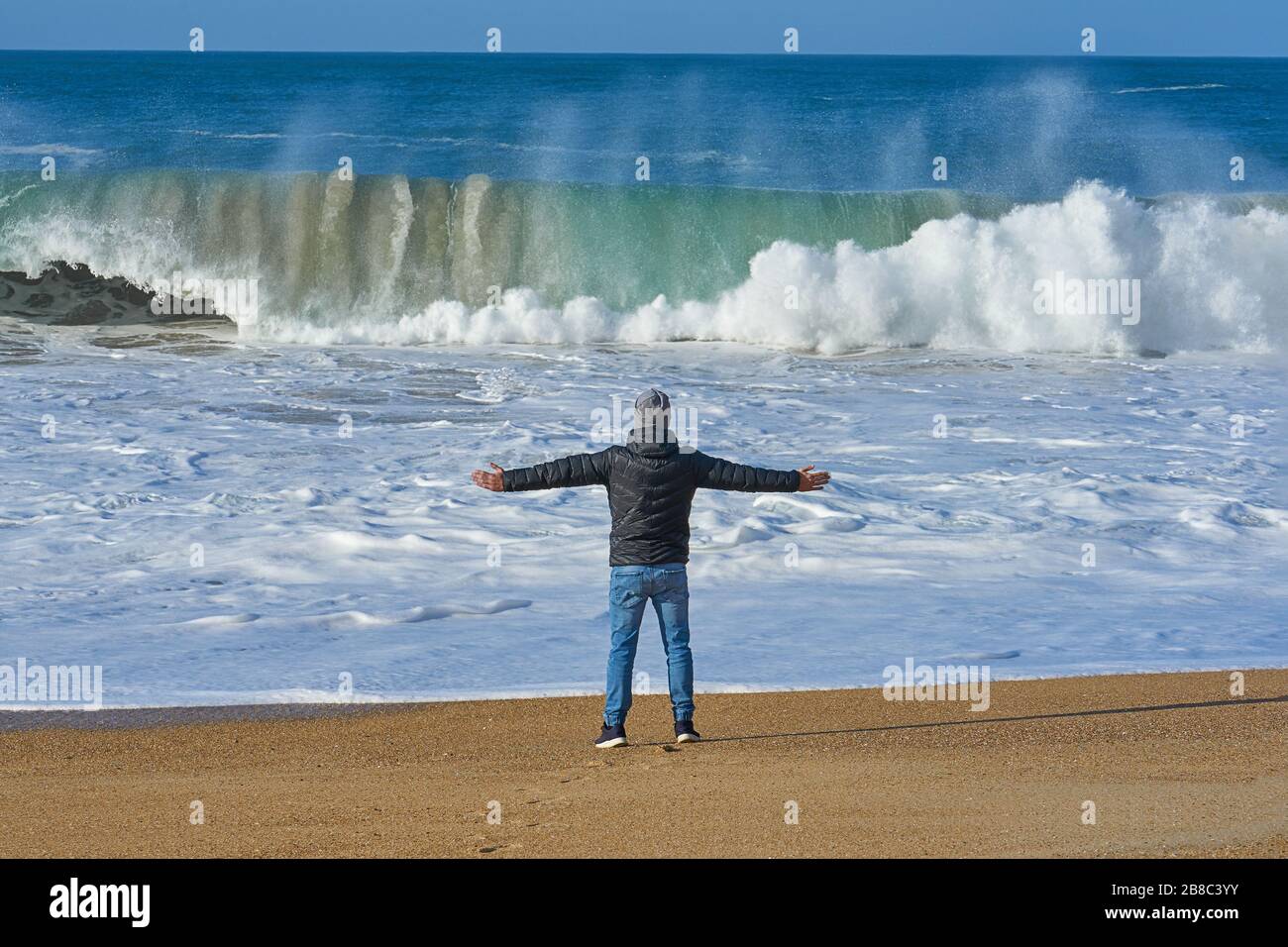 Rear view of man enjoying big wave of ocean on an empty sandy beach ...