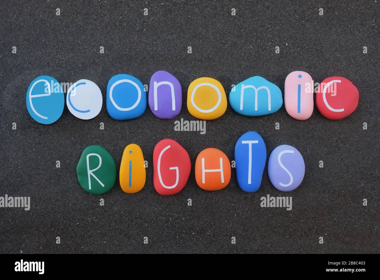 Economic rights, the right to an adequate standard of living text composed with multi colored stone letters over black volcanic sand Stock Photo