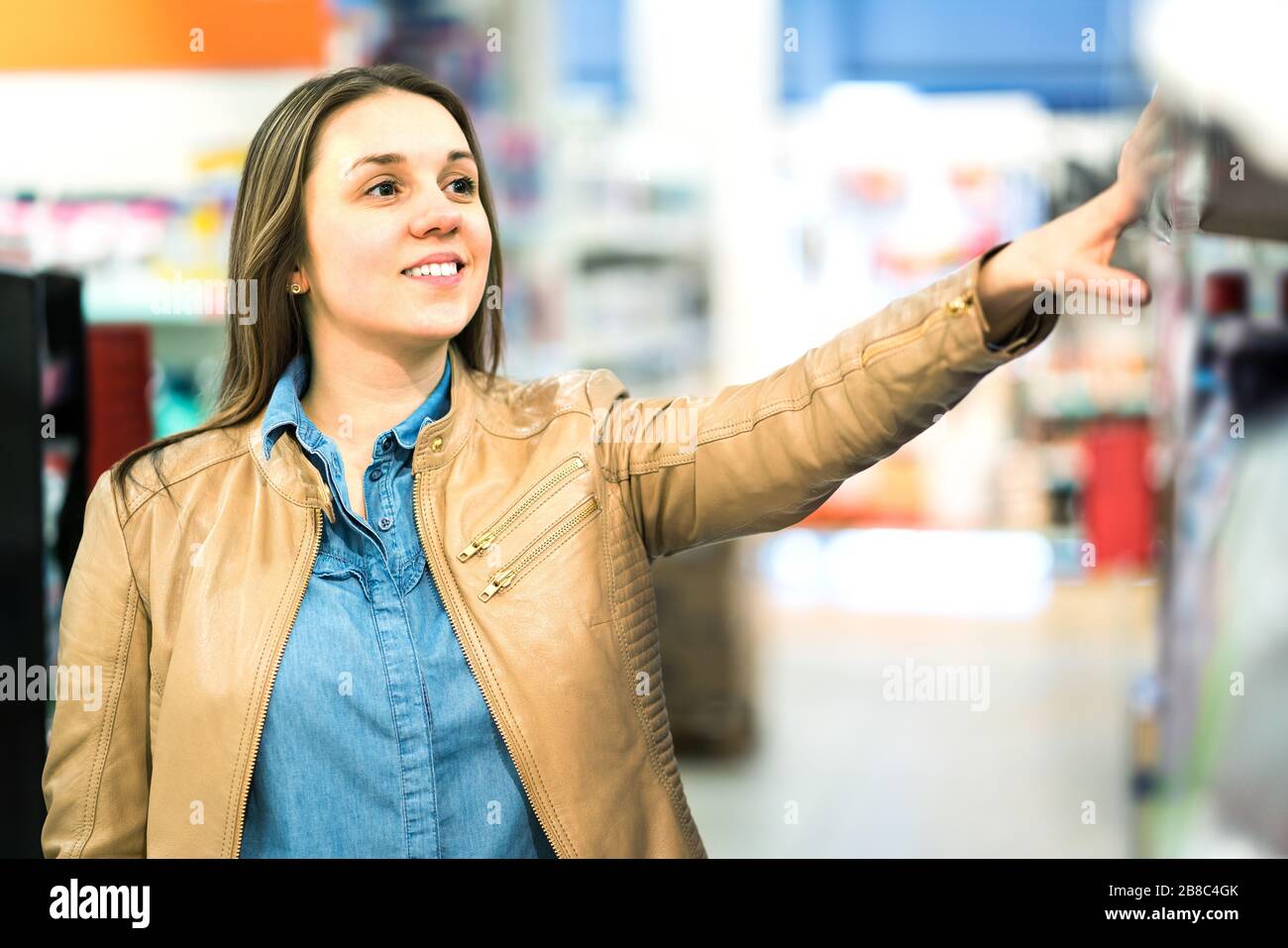 Woman at beauty product shelf in supermarket or buying medicine in pharmacy or drugstore. Smiling lady looking at cosmetics in shop aisle. Stock Photo