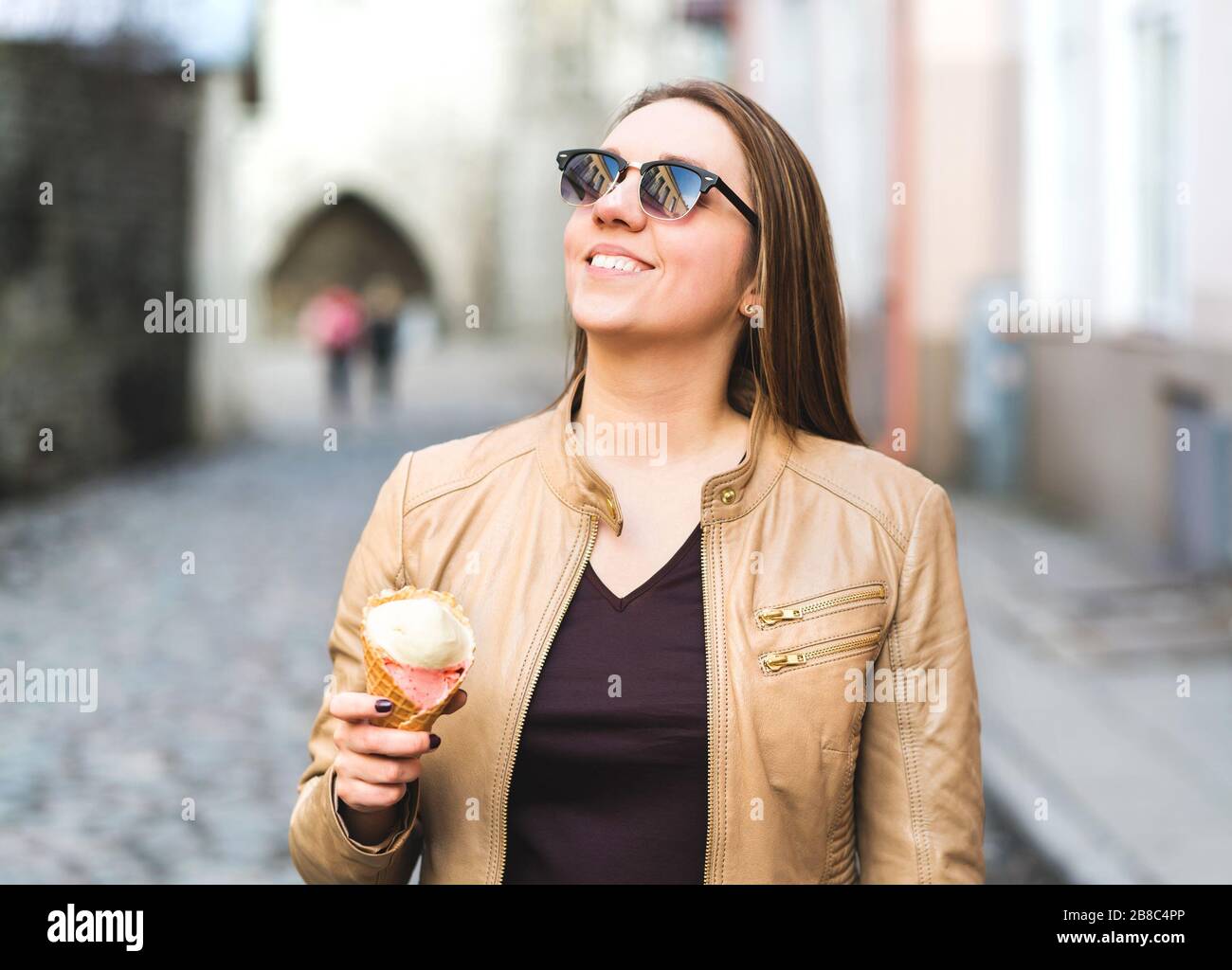 Happy woman eating and holding ice cream cone in city street. Smiling person enjoying her day off with delicious dessert. Stock Photo