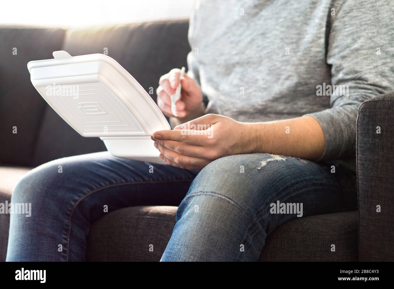 Man eating fast food from take away box home on couch. Takeout dinner from chinese or junk food restaurant. Guy enjoying kebab or salad. Stock Photo