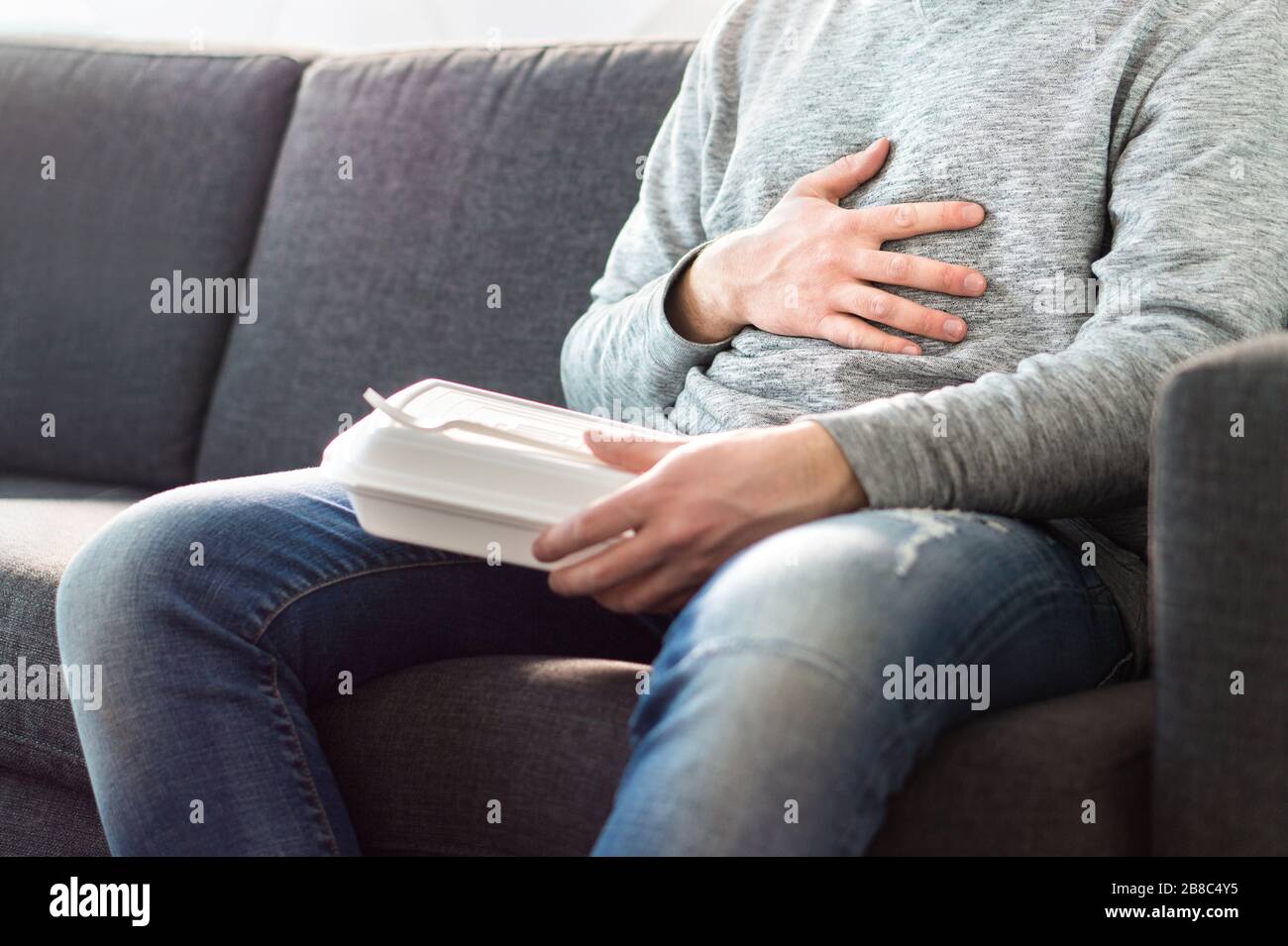 Stomach pain, food poisoning or digestion problem after fast junk food. Man ate too much and is holding belly with hand. Indigestion, heart burn. Stock Photo