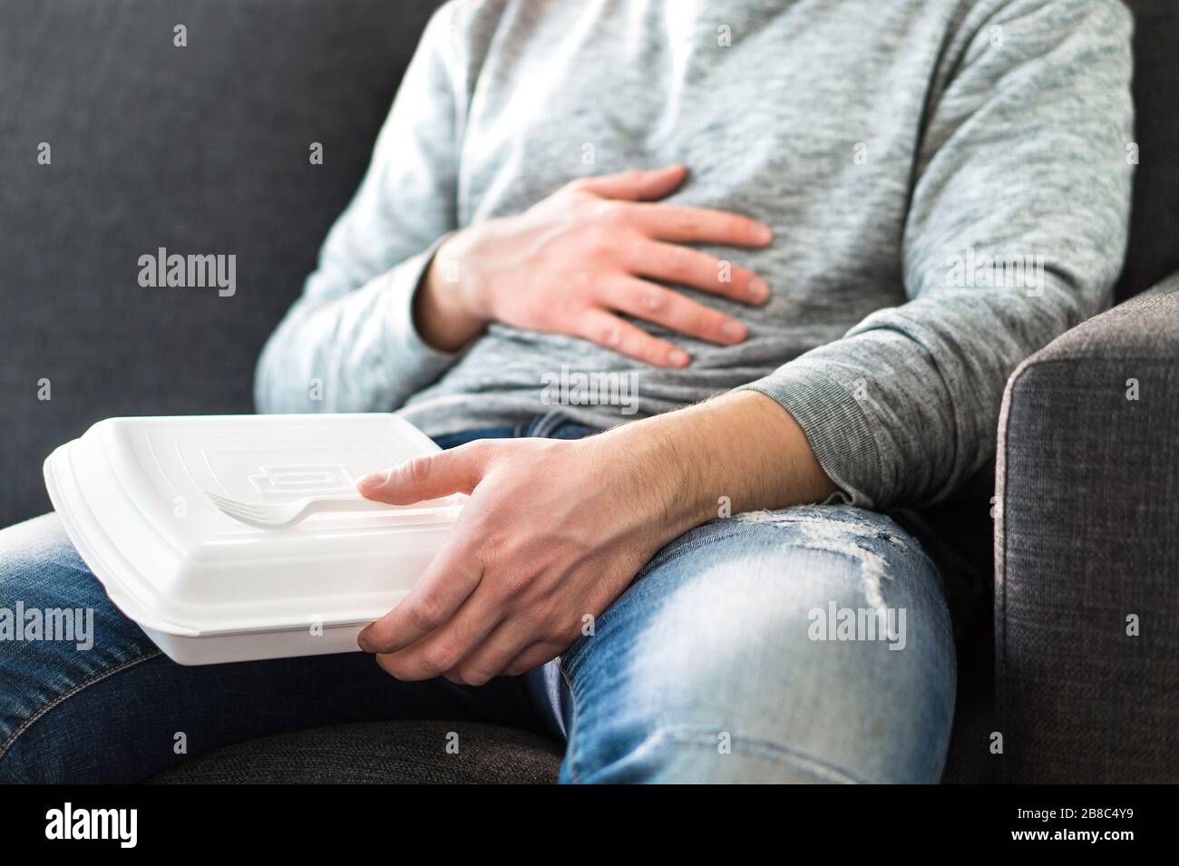 After eating fast food. Man feeling full or taking nap after eating junk. Guy having hangover or unhealthy diet. Stomach pain while sitting on couch. Stock Photo