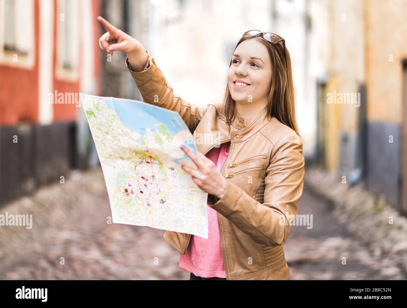 Tourist with map in the city. Woman pointing at right direction or showing attraction with finger. Happy traveler using tourism guide. Stock Photo