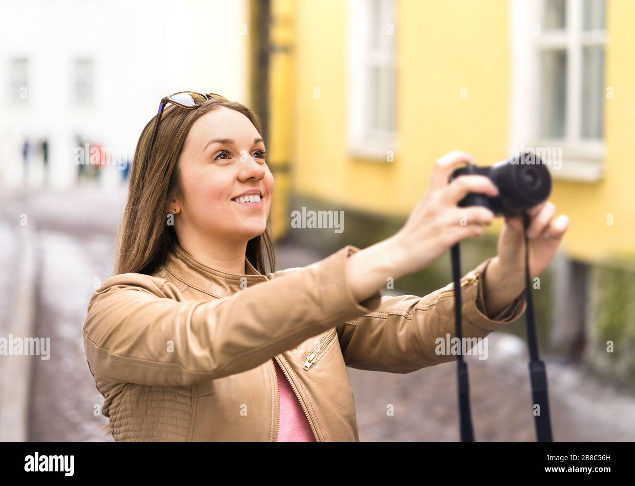Happy woman taking photo with camera. Tourist on vacation in city street. Holiday pictures. Smiling photographer or hobbyist. Stock Photo