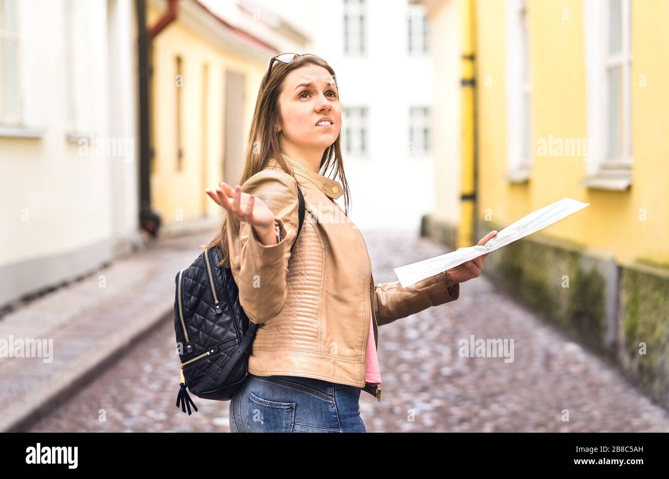 Tourist lost in the city. Confused woman holding map and spreading hands in old town. Disappointed and worried traveler having problem. Stock Photo