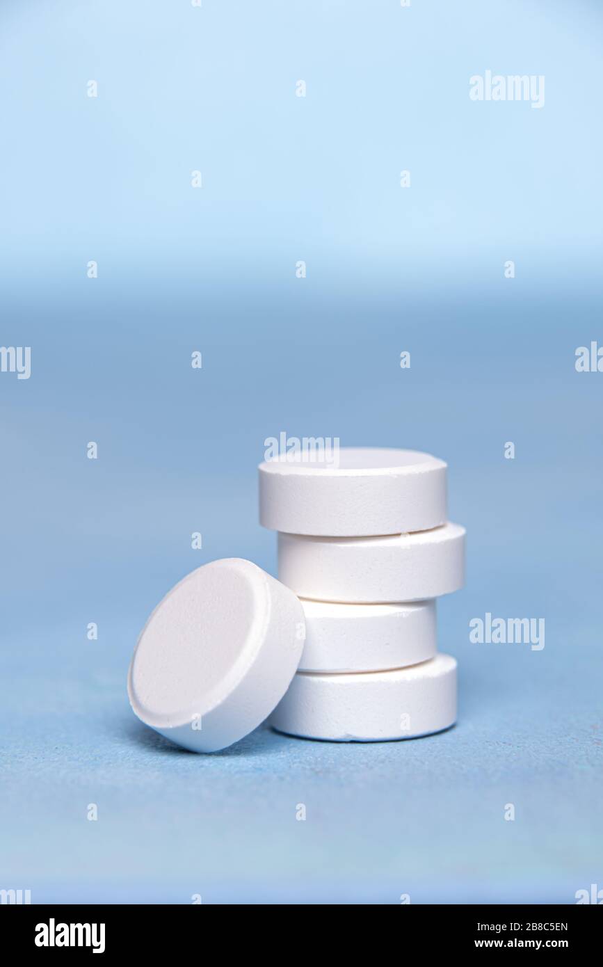 Close-up of large white round tablets of Vitamin C grouped in vertical pile on blue textured surface. One tablet is at the bottom of the pile. Selecti Stock Photo