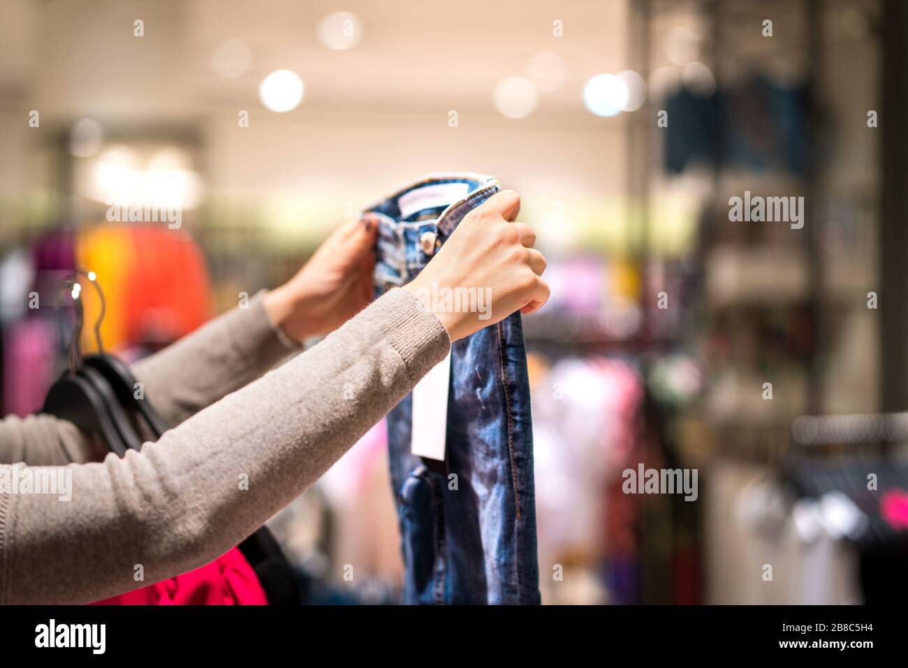 Woman holding jeans and shopping in fashion clothing store. Person choosing trendy skinny jeans in clothes shop. Stock Photo