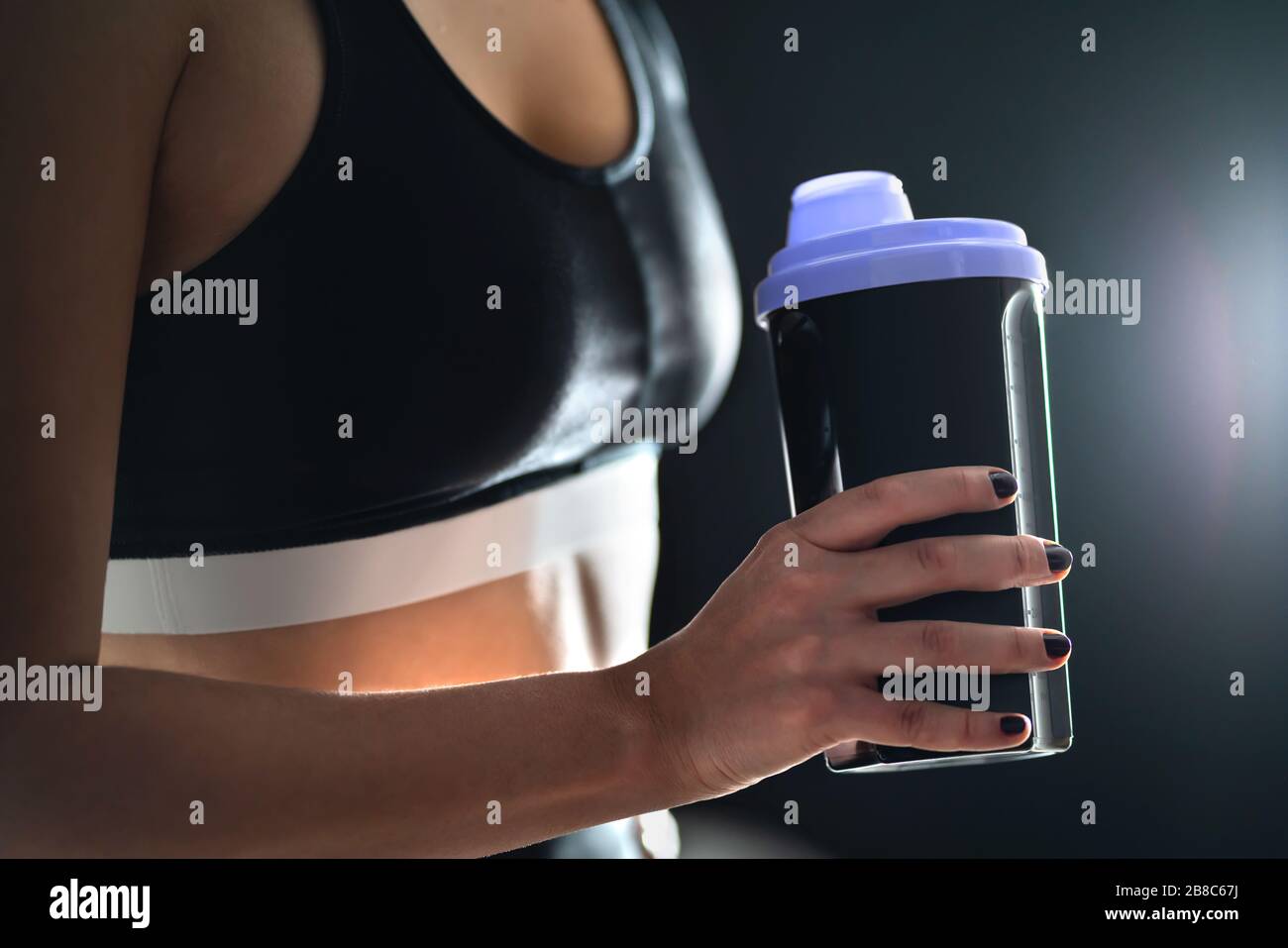 Protein shake after workout and gym training. Fit woman holding bottle of sport drink, whey or healthy smoothie. Fitness athlete with shaker. Stock Photo
