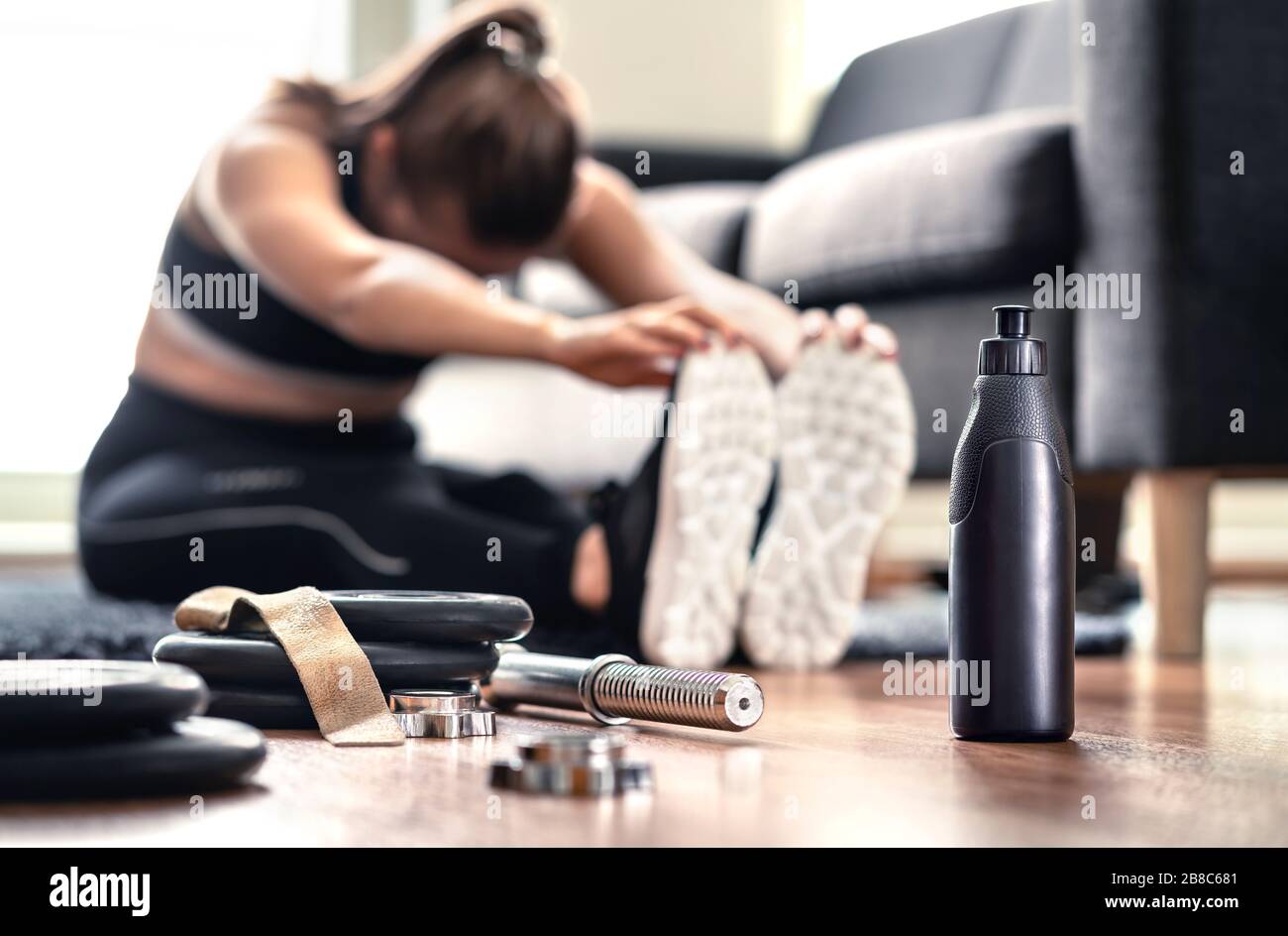 Woman stretching muscles before gym workout and weight training in home living room. Female fitness athlete doing warm up and physical exercise. Stock Photo