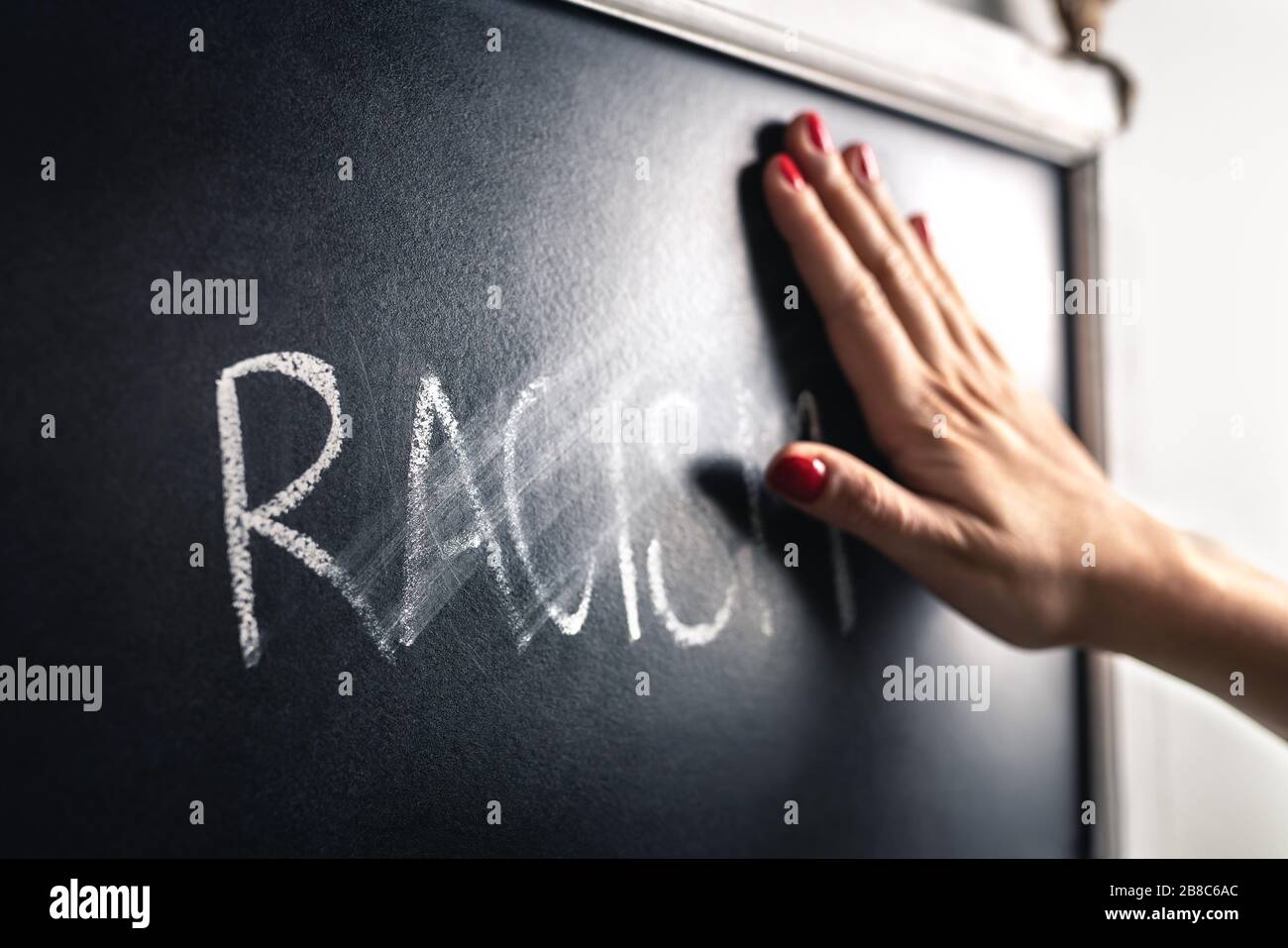 Racism concept. Stop hate and discrimination. Against prejudice and violence. Hand wiping off and erasing the word from blackboard. Stock Photo