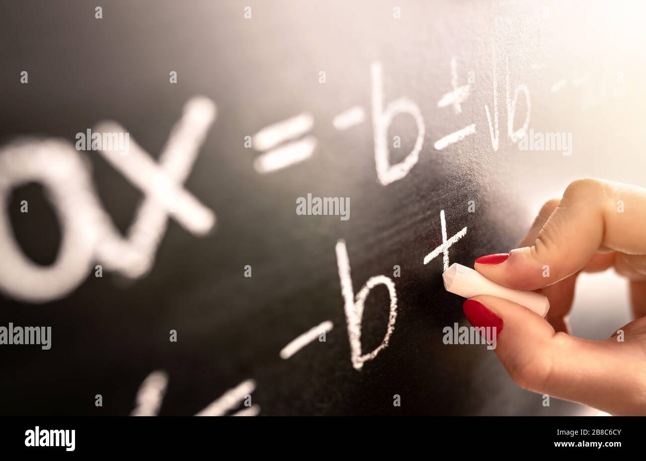 Math teacher writing function, equation or calculation on blackboard in school classroom. Student calculating on chalkboard. Stock Photo