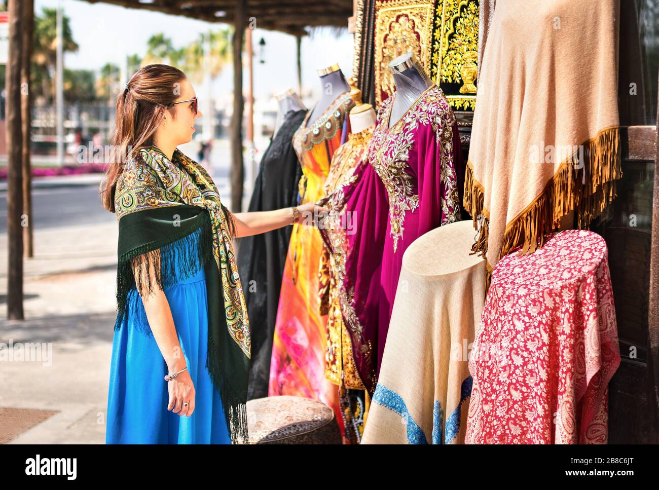 Woman in souk. Tourist looking at traditional Arabian dresses and clothes in store or outdoor market. Lady customer shopping souvenir in old Dubai. Stock Photo