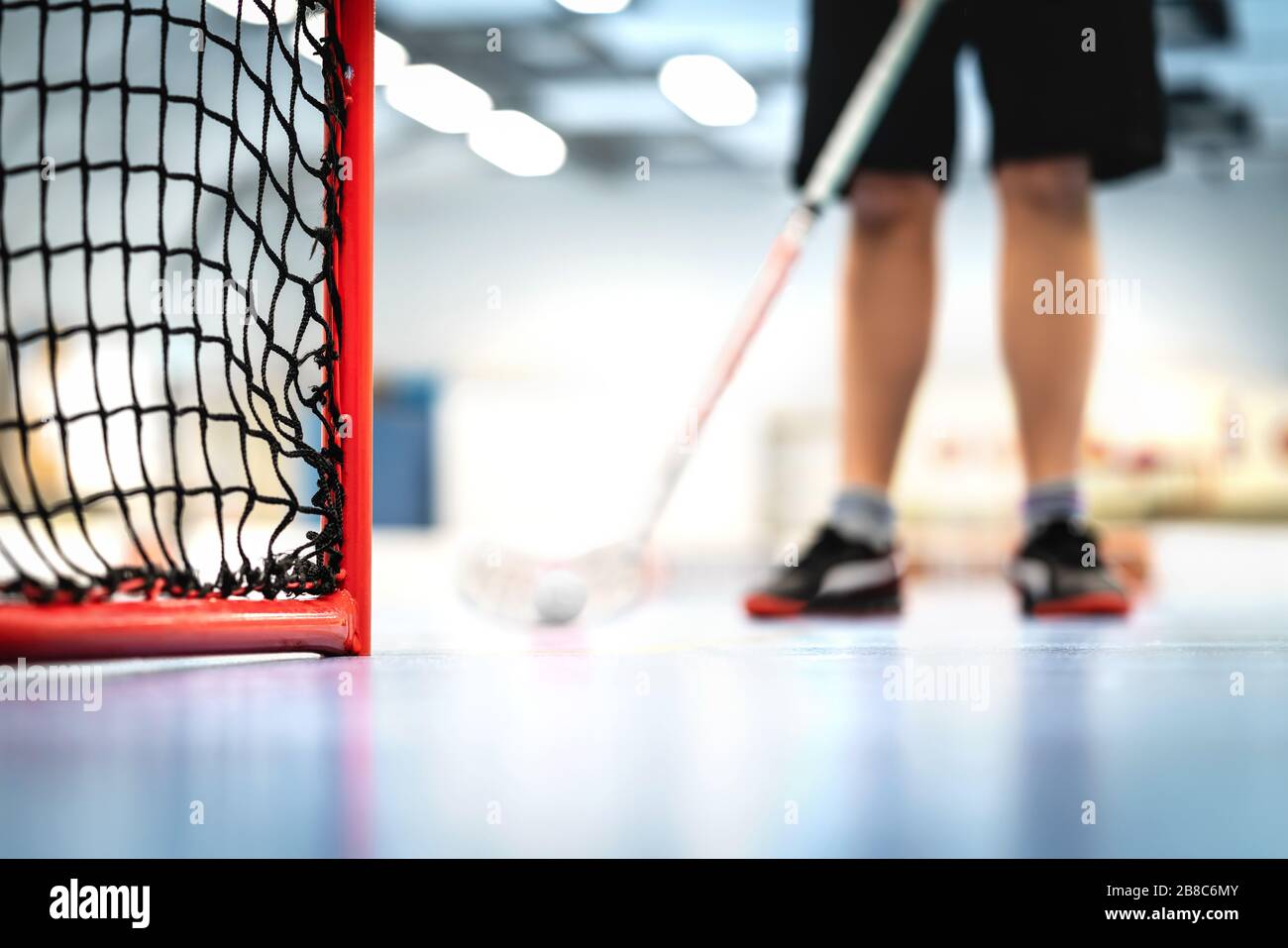 Floorball goal and net. Player training in the background. Man playing floor hockey on court. Stock Photo