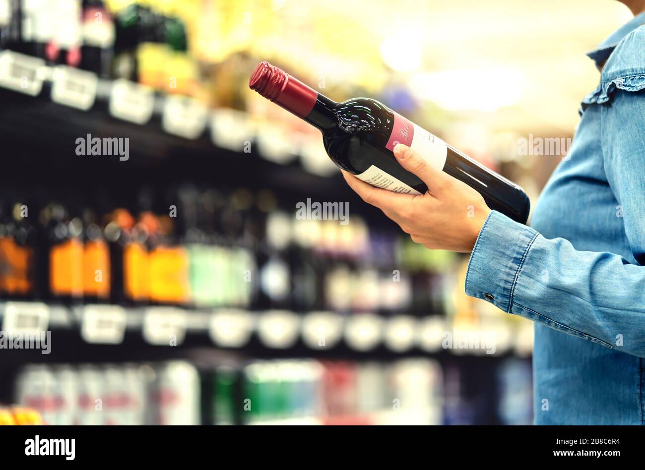Alcohol shelf in liquor store or supermarket. Woman buying a bottle of red wine and looking at alcoholic drinks in shop. Stock Photo