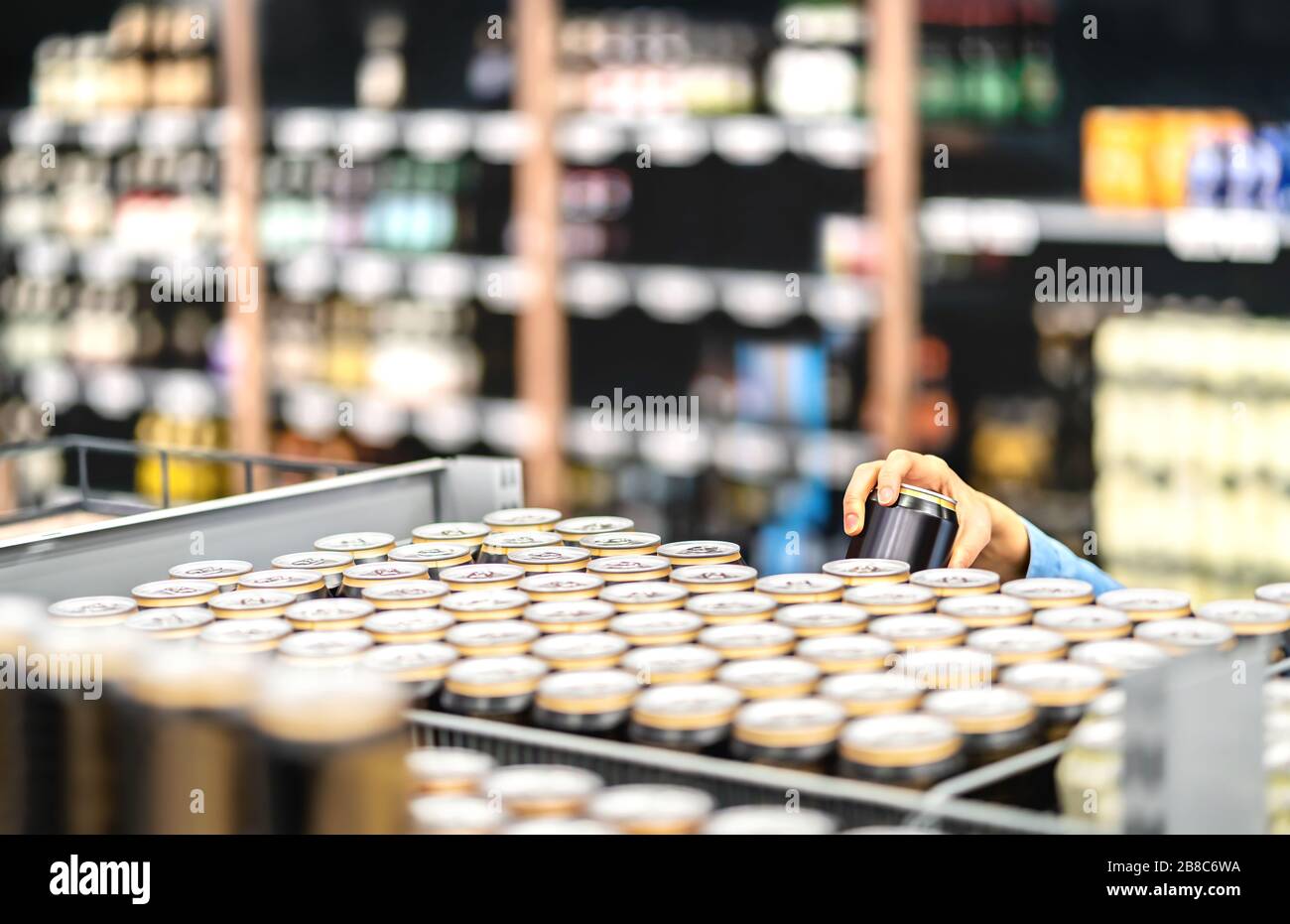 Retail worker filling shelf with drinks in grocery store or customer taking can of beer or soda. Staff at supermarket stocking shelf with alcohol. Stock Photo