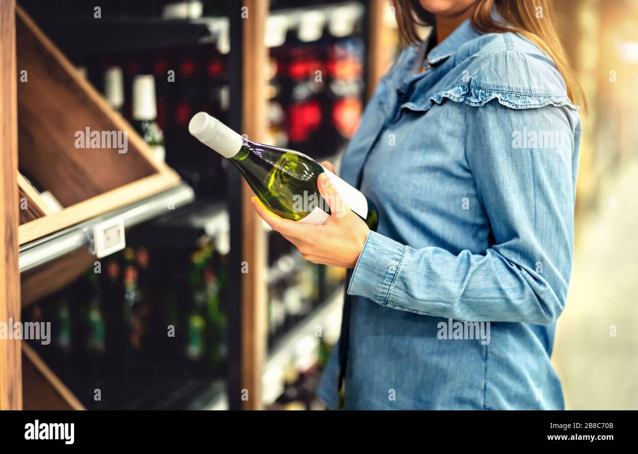 Customer buying white wine or sparkling drink. Alcohol aisle in store or supermarket. Woman holding bottle. Buying riesling or chardonnay. Stock Photo