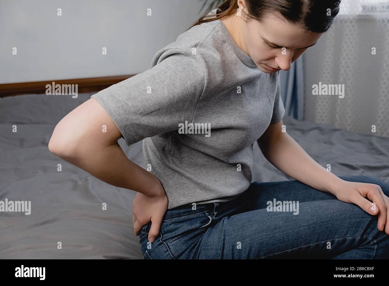 Upset young woman suffering from backache after sleep, rubbing stiff muscles, unhappy girl sitting on bed at room, feeling discomfort, because of bad Stock Photo