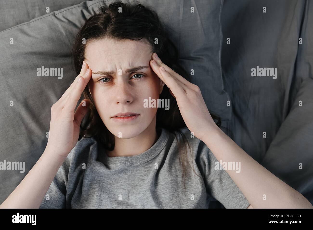 Unhappy thoughtful young woman holding hands on forehead, feeling sad lonely lying in bed alone trying to sleep thinking of problem, fears, worries an Stock Photo