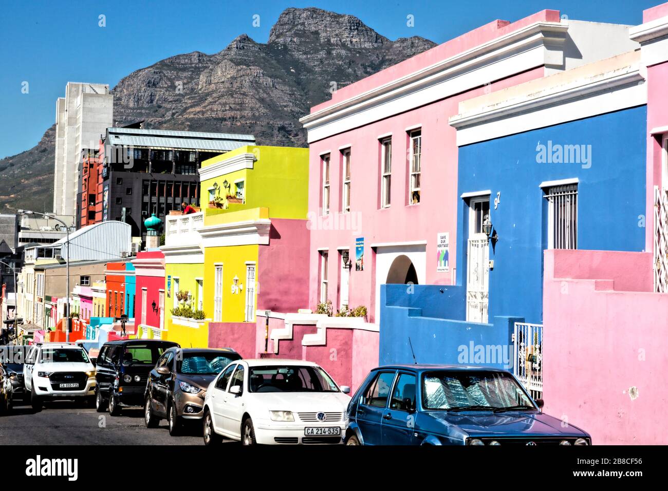 View down the brightly coloured facades of the houses of Wale Street to Buitengracht Street. Across the traffic and buildings, Devil's Peak looks down. Stock Photo