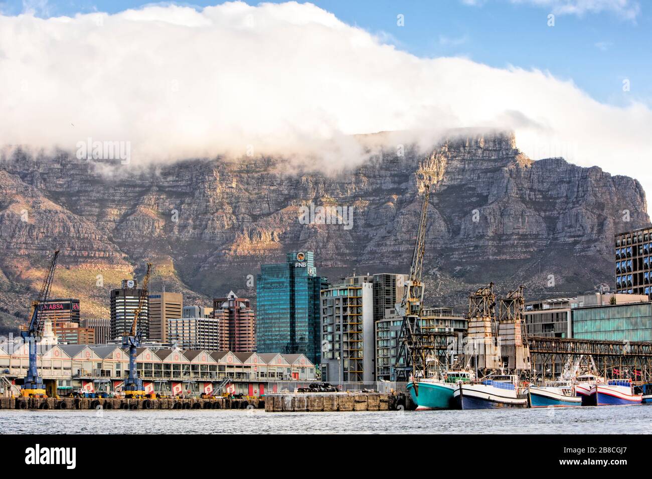 Docks, warehouses and fishing boats of Table Bay Harbour form the frontpiece to the Central Business District behind; all dominated by Table Mountain Stock Photo