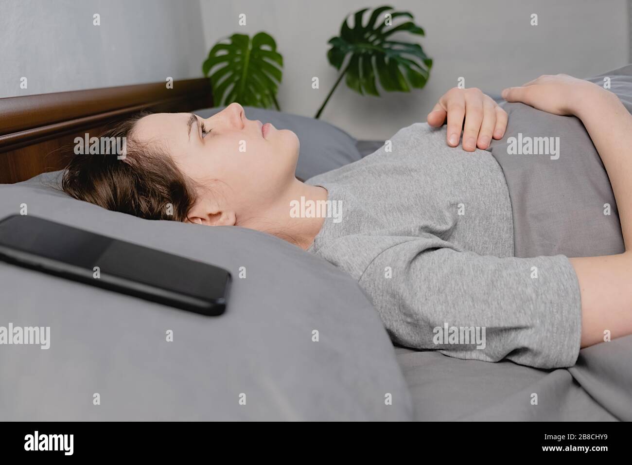 Young frustrated woman lying down on bed with phone looks into the