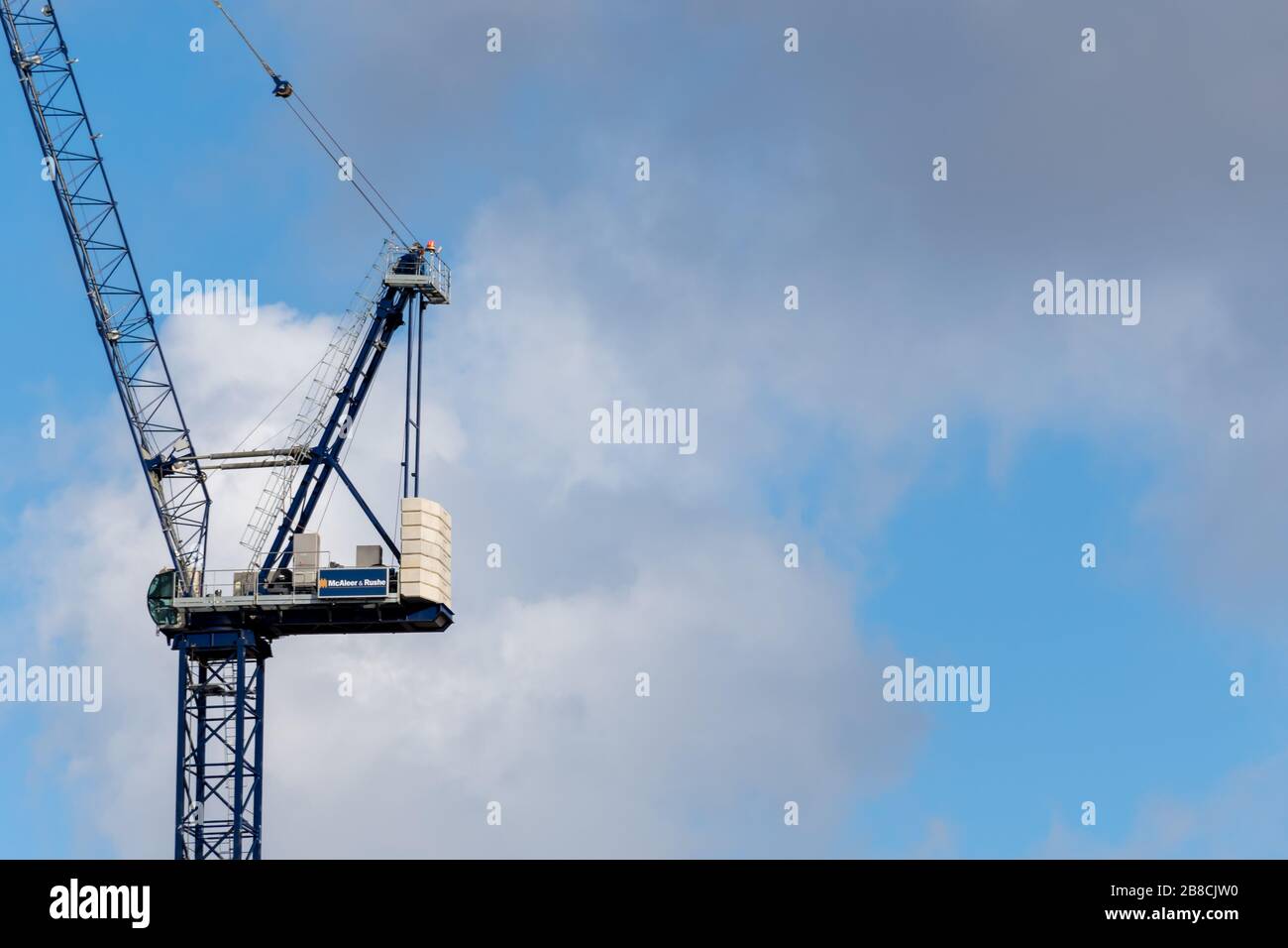 A blue tower crane high in the sky as a rain cloud approaches