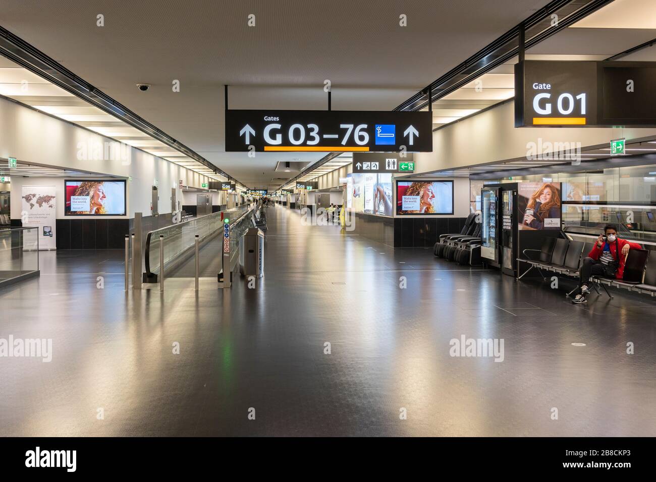 Empty gates at Terminal 3, Vienna Airport, deserted during the Coronavirus Covid 19 pandemic, 15th March 2020. A single person sits wearing a facemask Stock Photo