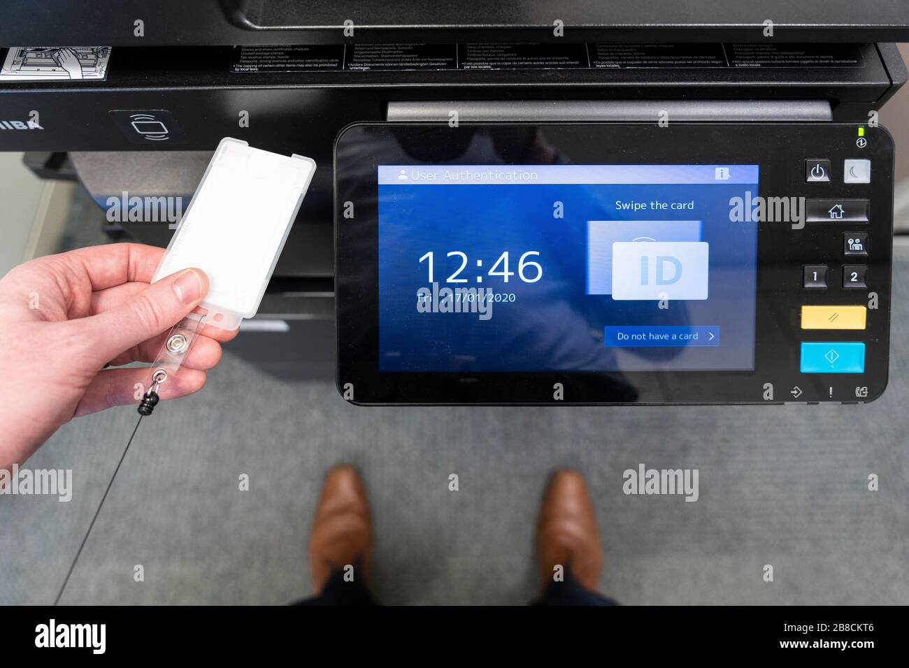 A person standing at a printer and using a security swipe card to log onto a printer in an office. Theme: office work, mundane, daily grind, 9 til 5 Stock Photo