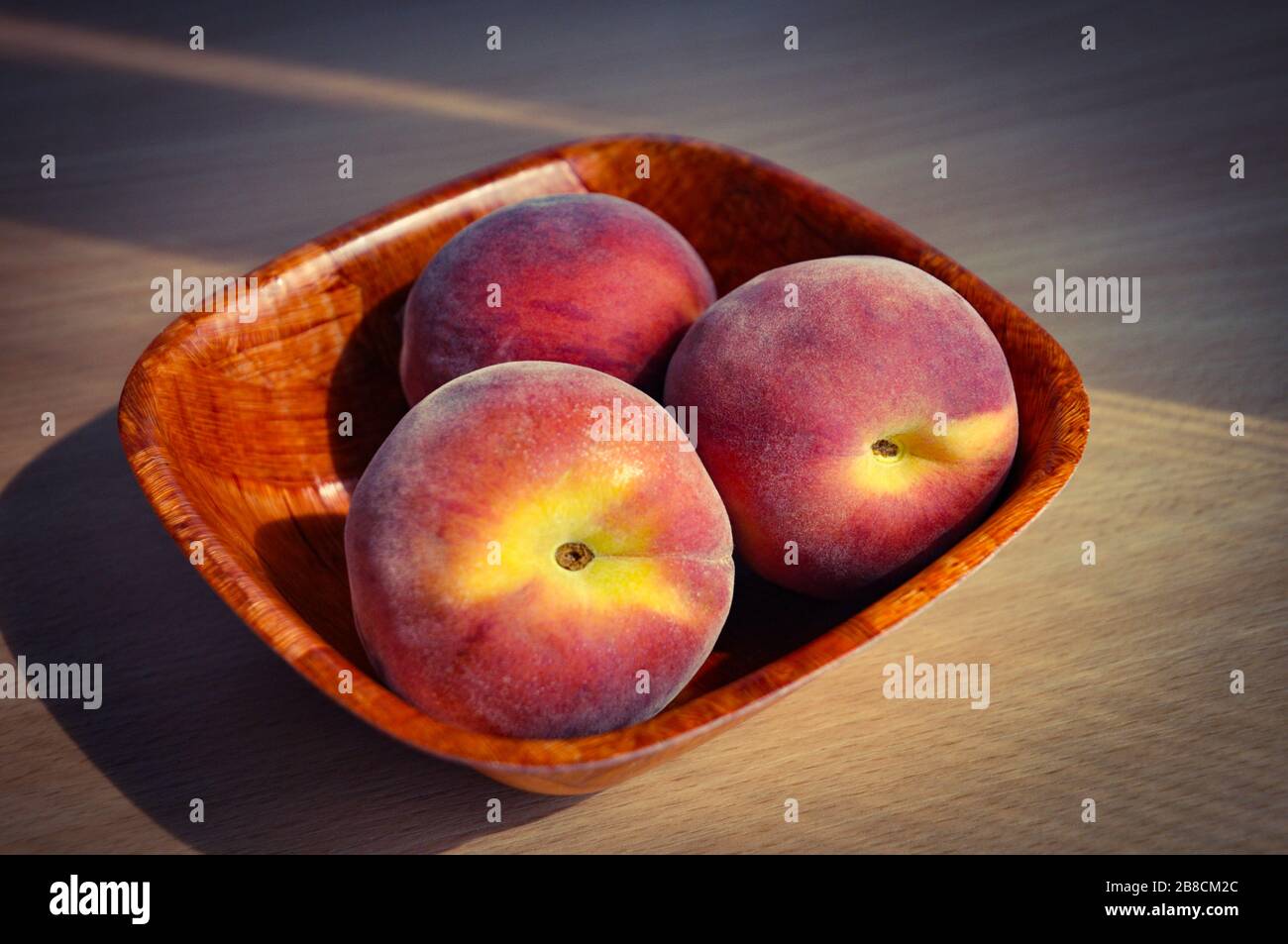 Still life with wooden bowl with three ripe peaches Stock Photo