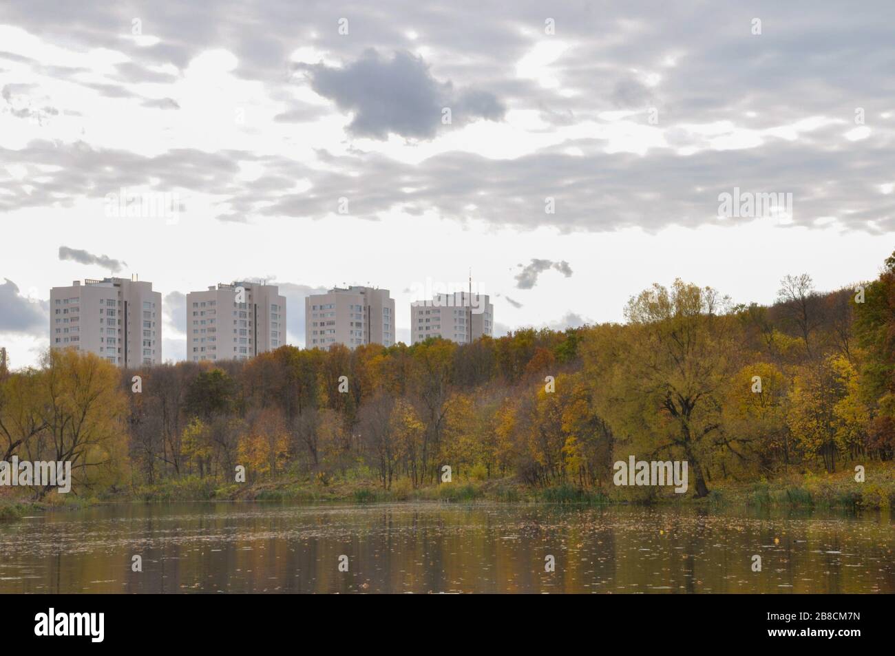 Landscape in cloudy october day with pond and trees in the foreground and several multi-storey buildings in the background. Stock Photo