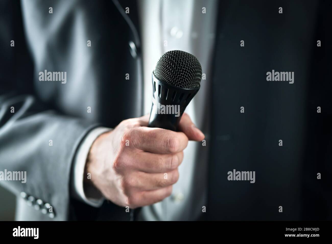 Business man holding microphone. Public speaking and giving speech in suit for audience concept. Fiance, host or best man giving toast with mic. Stock Photo