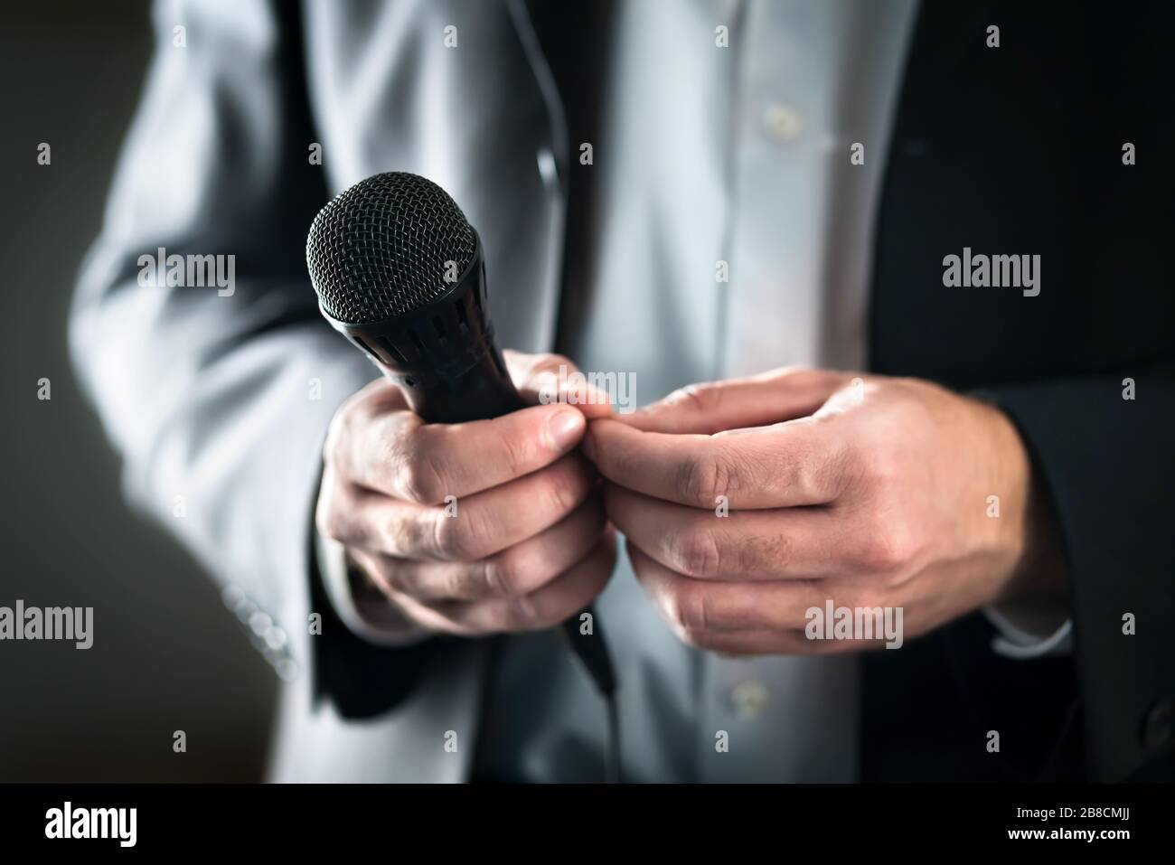 Stage fright concept. Nervous and shy public speaker with microphone. Business man afraid of giving speech for crowd of people or audience. Stock Photo