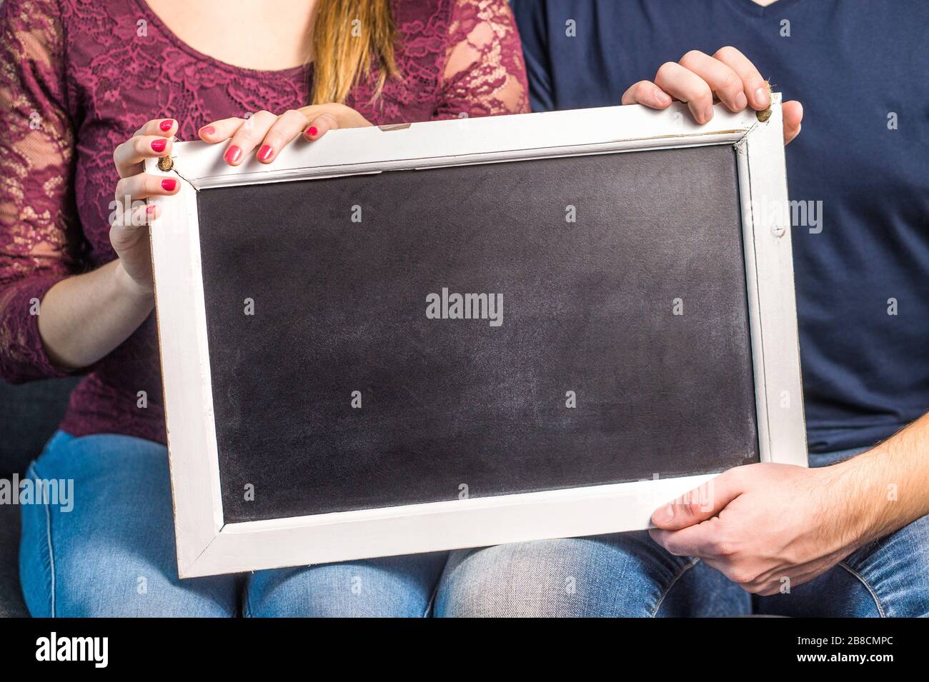 2 people holding empty chalkboard with wooden frame. Friends or a couple showing blank blackboard with copy space for background. Stock Photo