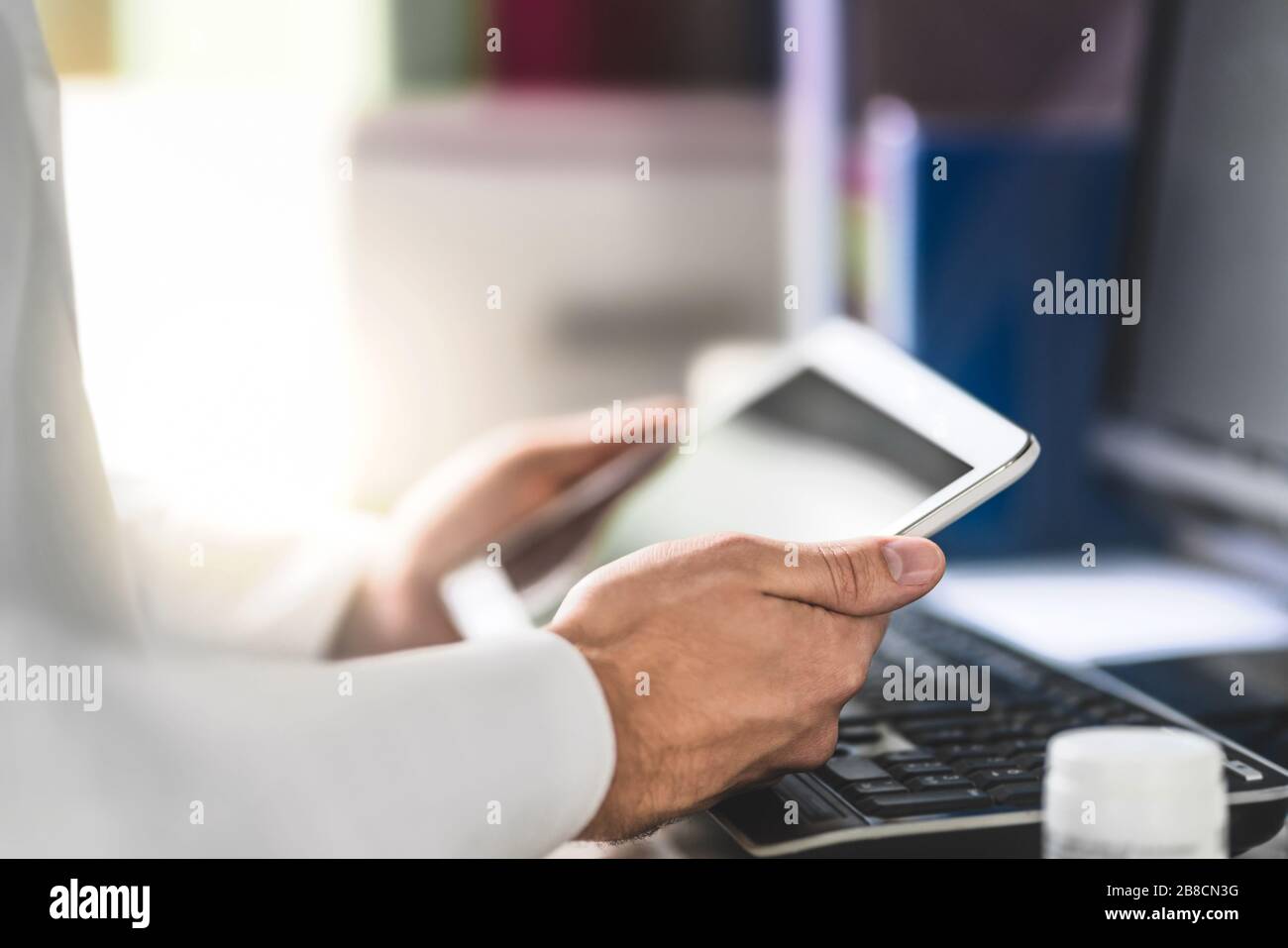 Doctor holding tablet in hand and reading medical record of patient. Physician using mobile device in office room. Stock Photo