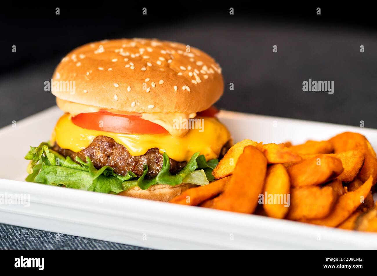Burger meal on plate. Delicious hamburger with juicy beef, melting cheddar cheese served with crispy sweet potato fries. Home cooking. Stock Photo