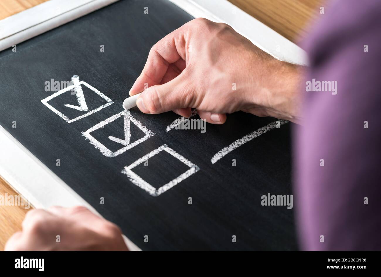 Man writing checkmark to checklist on blackboard. Document of finished work and completed tasks on chalkboard. Check list for planning. Stock Photo