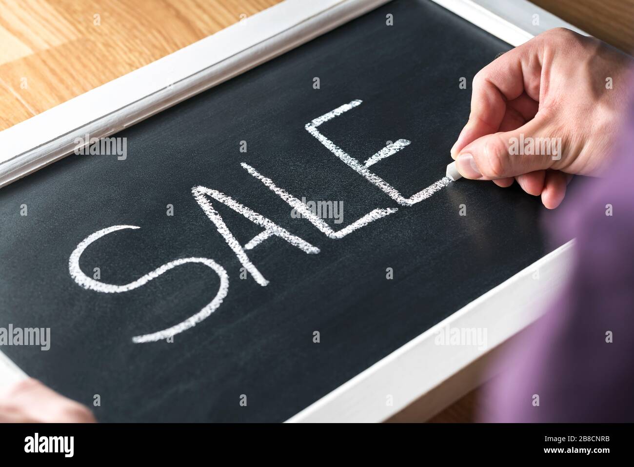 Sale blackboard banner in store, shop or marketplace to promote bargain prices or clearance. Small business owner, salesman or assistant writing text. Stock Photo
